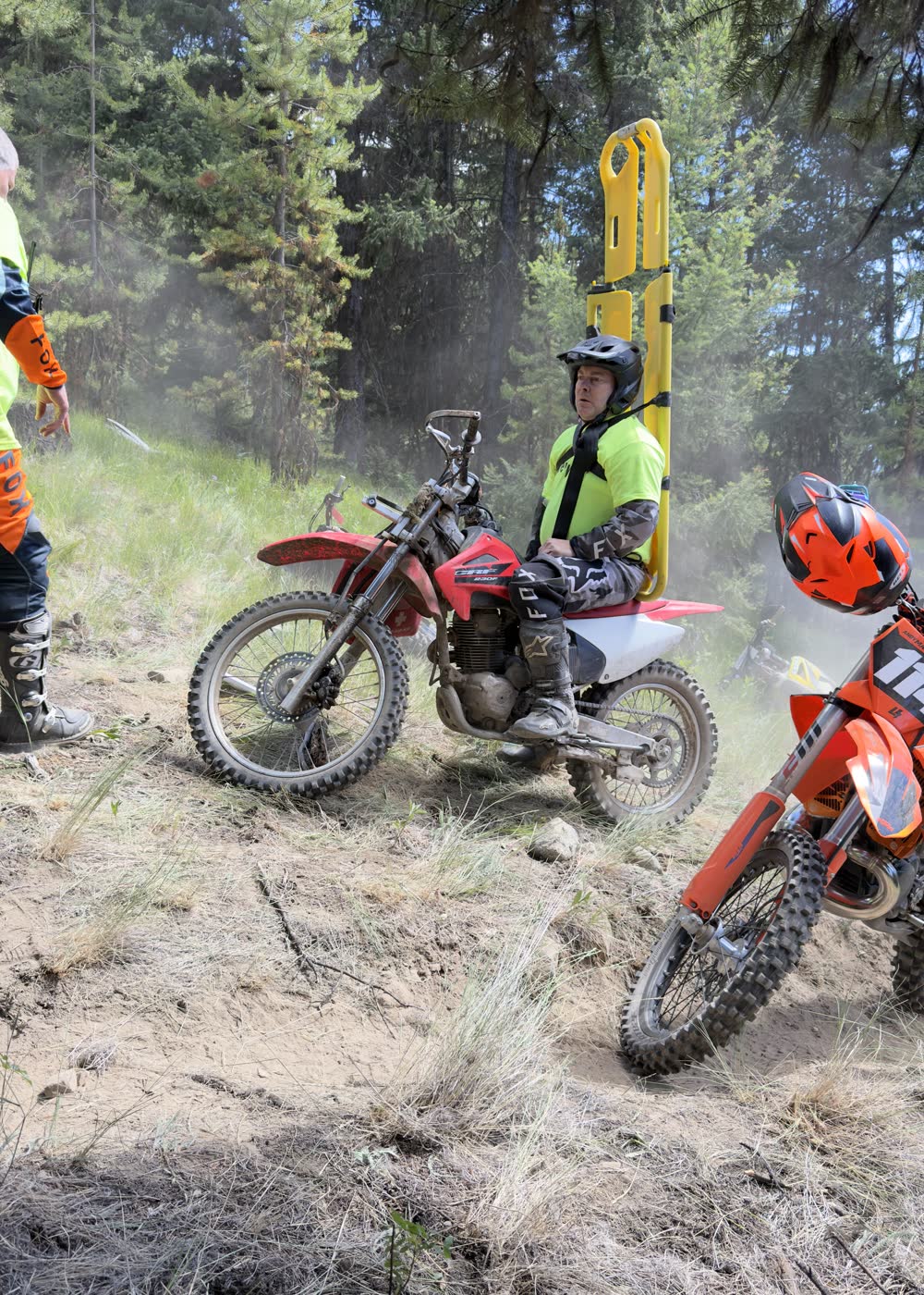 A medic carrying a spine board on a dirt bike, riding in to reach an injured rider on a remote trail.